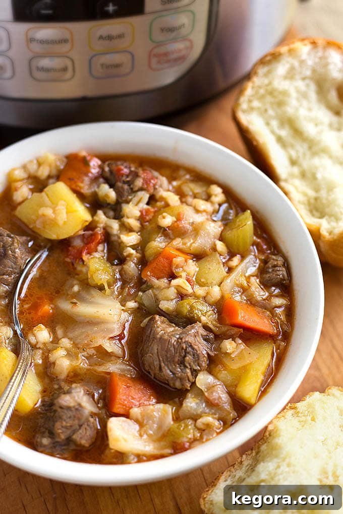 The Most Beloved Instant Pot Dishes of 2017 15 A steaming bowl of Instant Pot Beef Barley Vegetable Soup, served in a white bowl with a spoon, accompanied by fresh rolls and a pressure cooker in the background.