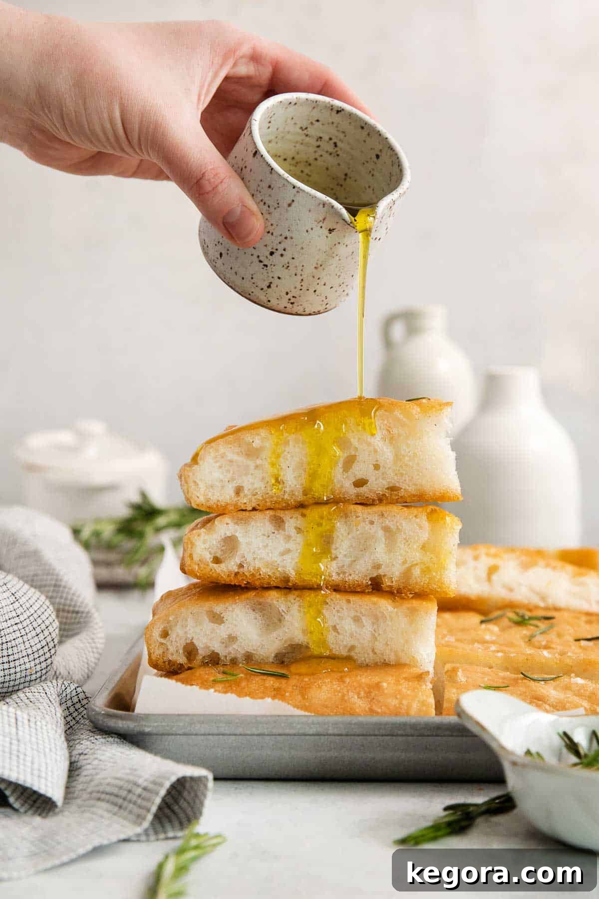 No Knead Overnight Gluten Free Focaccia with Caputo Flour 8 Olive oil being poured over a stack of freshly baked gluten-free focaccia slices.