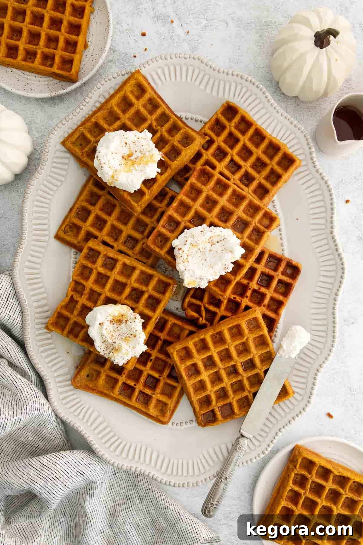 Fluffy Gluten-Free Pumpkin Waffles 3 Golden brown gluten-free pumpkin waffles stacked on a white platter, adorned with generous dollops of whipped butter and a drizzle of maple syrup.