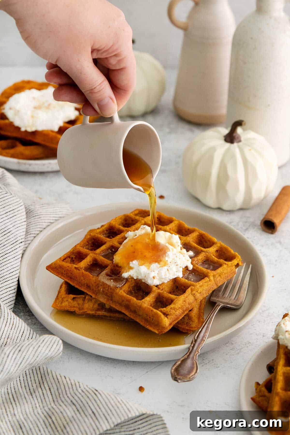 Fluffy Gluten-Free Pumpkin Waffles 7 Golden pumpkin waffles topped with whipped butter, being drizzled with rich maple syrup on a white plate, ready to be enjoyed.