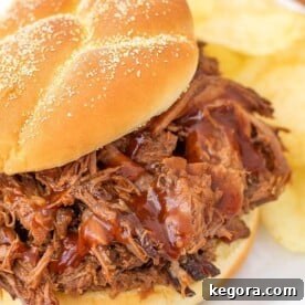 Instant Pot BBQ Pot Roast 5 Barbecue Beef on a hamburger bun with potato chips on a white plate