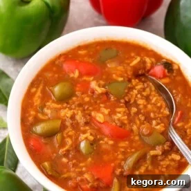 Stuffed Pepper Soup in white bowl with spoon with green and red bell peppers in background