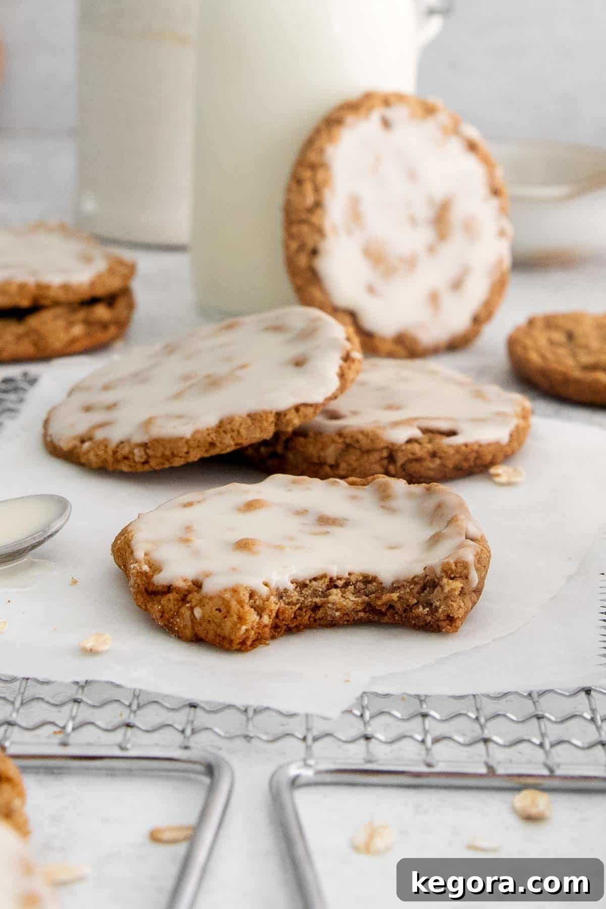 Irresistible Gluten-Free Iced Oatmeal Cookies 3 Beautifully iced gluten-free oatmeal cookies arranged on parchment paper and a wire rack, with one cookie showing a missing bite.