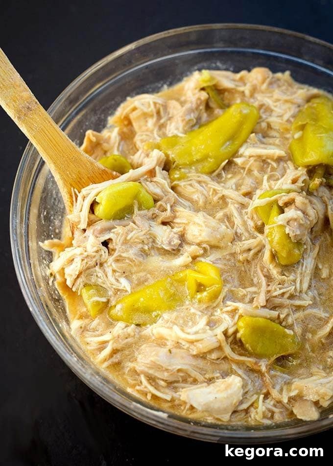 Delicious Mississippi Chicken in a clear glass bowl, ready to be served, with a wooden spoon resting in it.