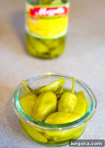 Small glass bowl filled with vibrant green pepperoncinis, showing their distinctive wrinkled texture.