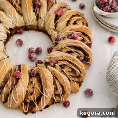 A vibrant gluten-free cinnamon roll wreath, richly glazed and garnished with festive sugared cranberries, ready to be served.