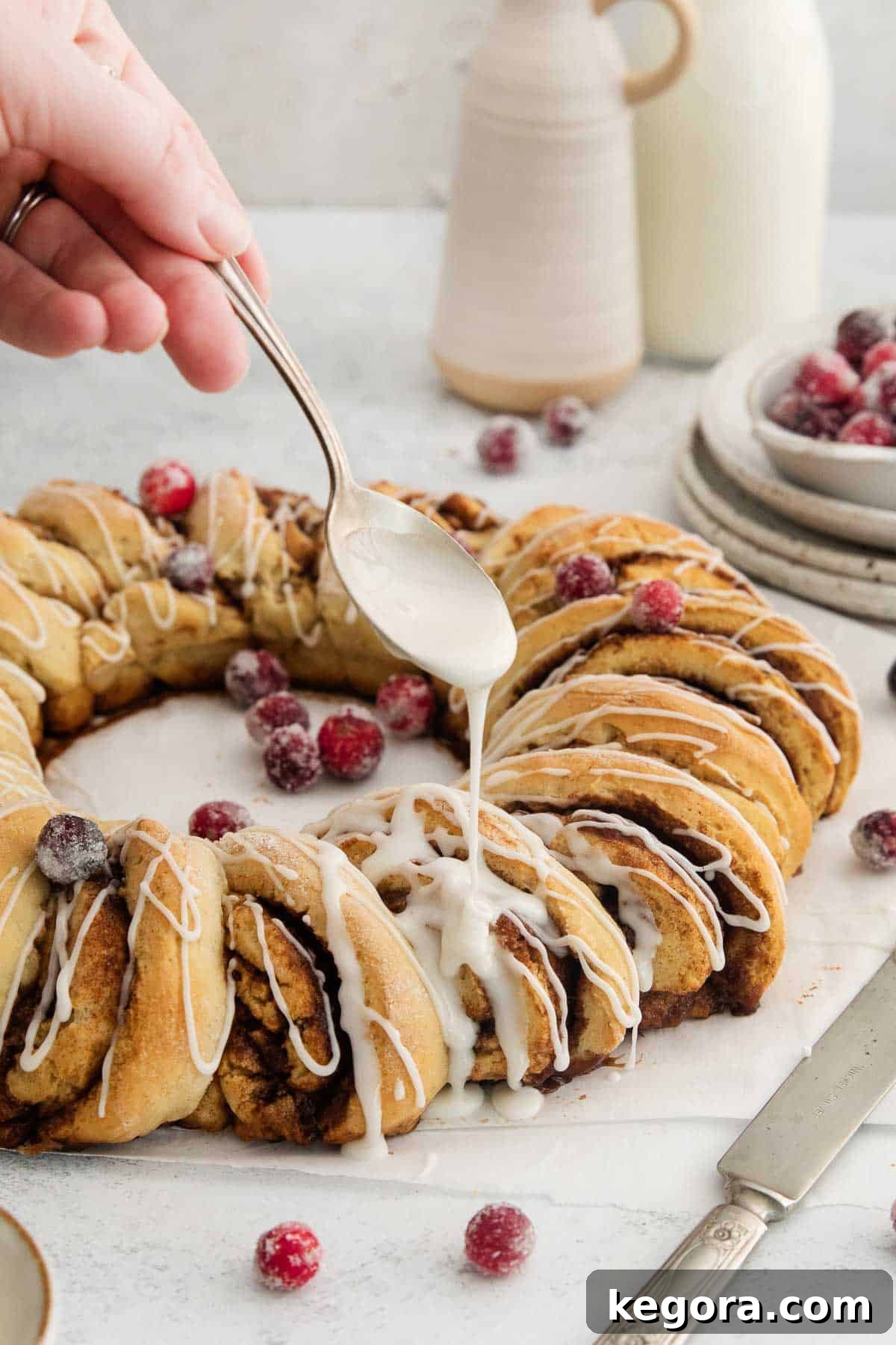 Irresistible Gluten-Free Cinnamon Swirl Wreath 9 Close-up shot of a thick, sweet glaze being delicately poured from a spoon onto the warm gluten-free cinnamon roll wreath, resting on parchment paper.