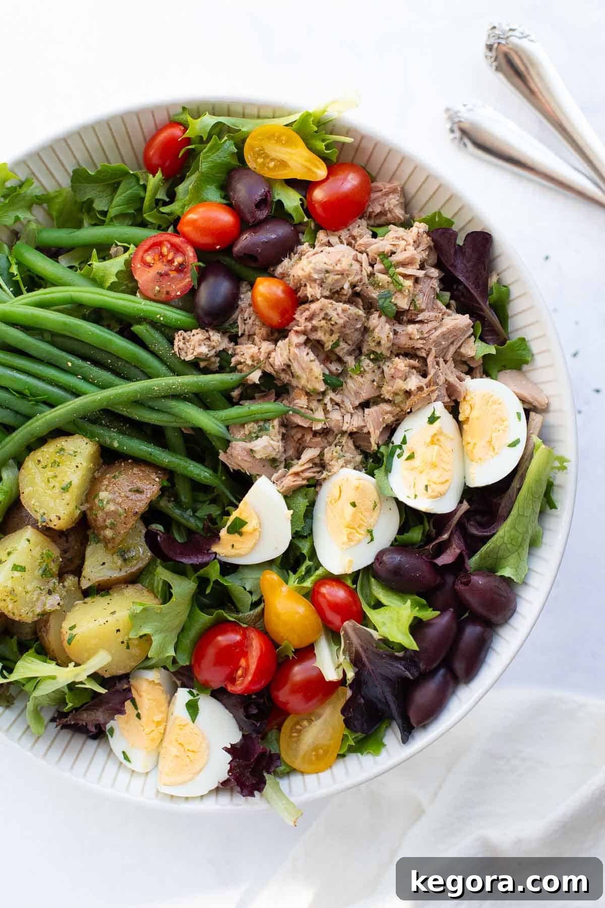 Salad Nicoise A vibrant Salad Niçoise served in a bowl with serving utensils, ready to be enjoyed.