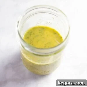 Classic Niçoise Vinaigrette 5 Homemade Niçoise salad dressing in a clear glass mason jar, showcasing fresh herbs.