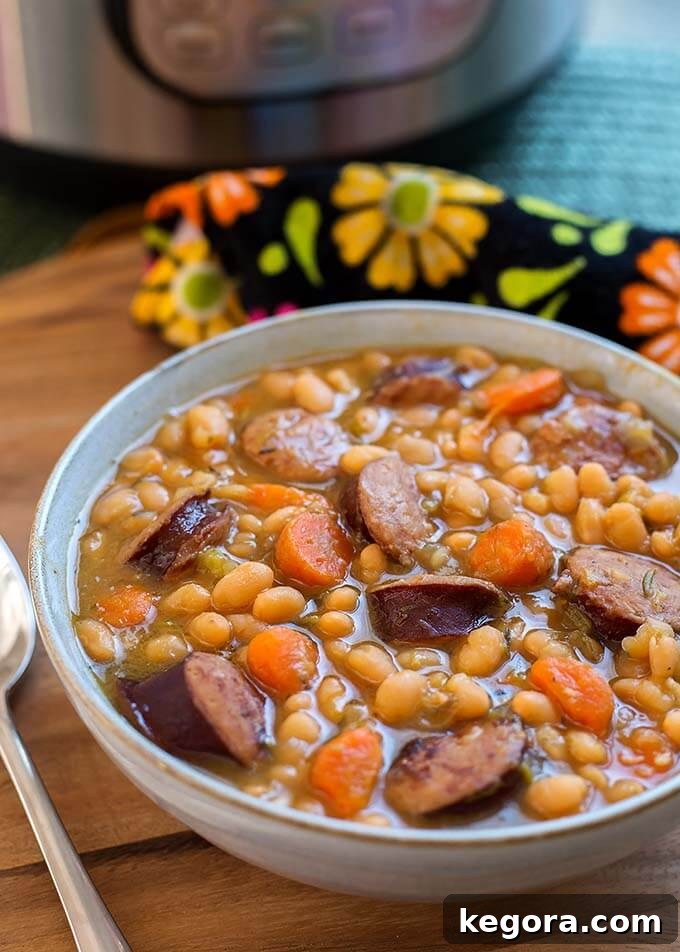 Sausage and White beans in a gray bowl next to a silver spoon on a wooden board