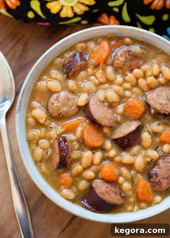 Sausage and White beans in a gray bowl next to a silver spoon on a wooden board