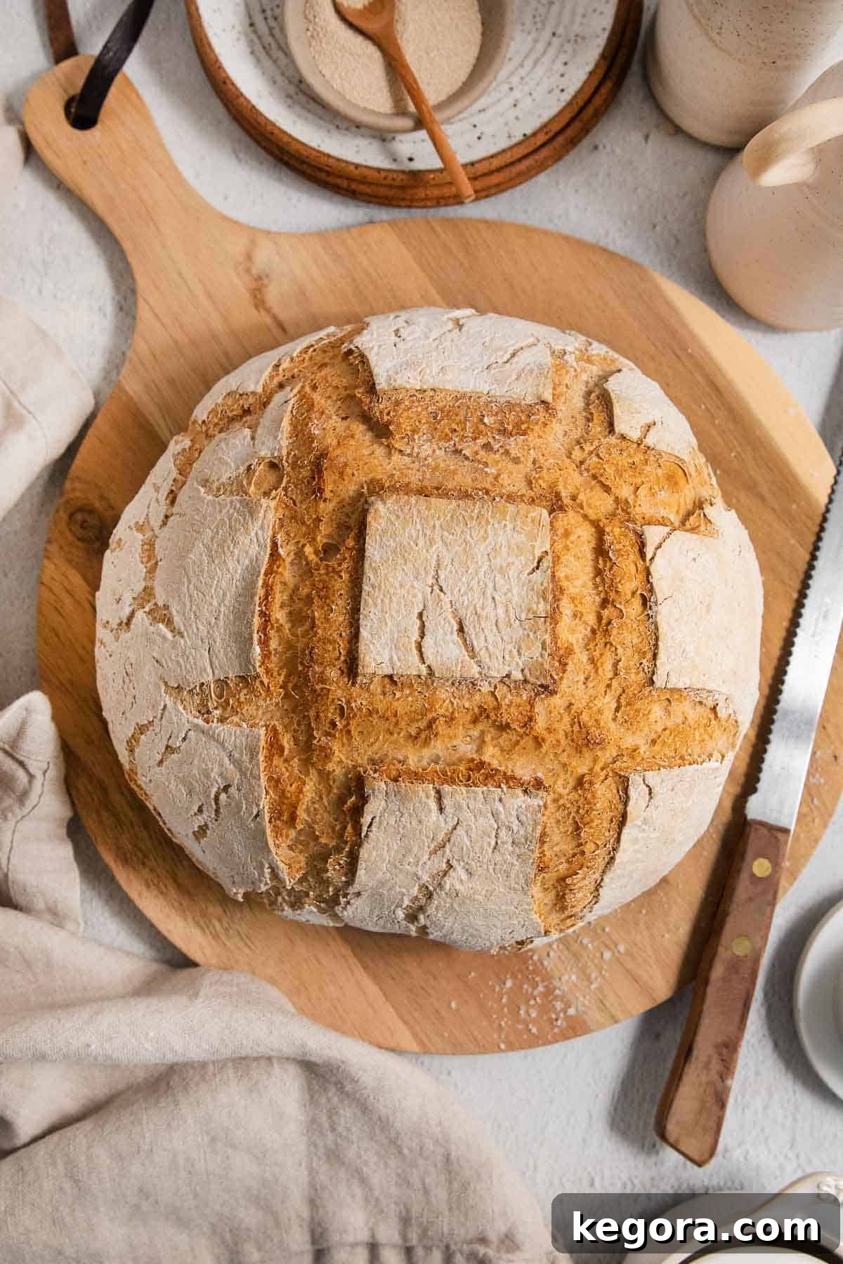 A perfectly baked artisan bread loaf resting on a rustic wooden board, accompanied by a bread knife, highlighting its golden crust and inviting texture.