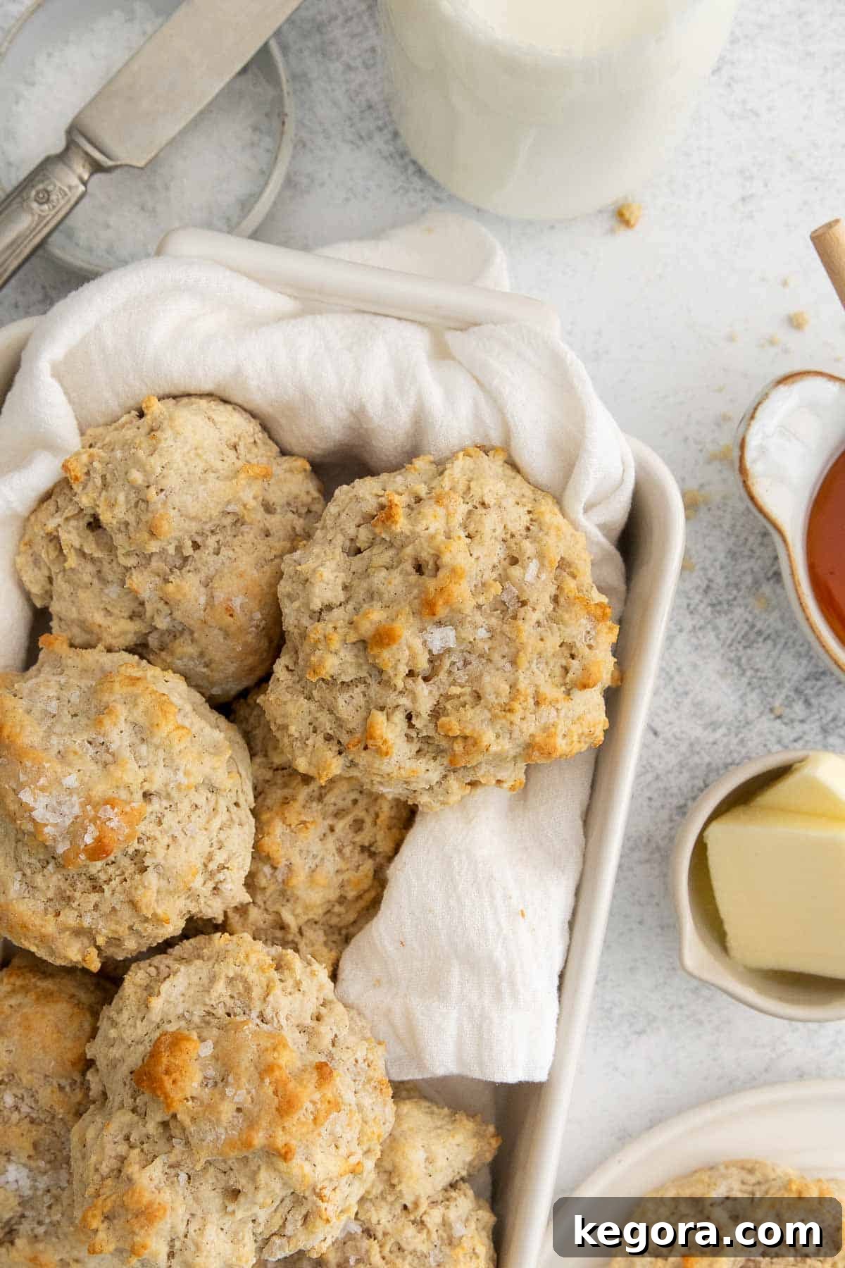 Golden-brown gluten-free drop biscuits arranged on a tea towel in a baking dish, with butter and honey on the side.