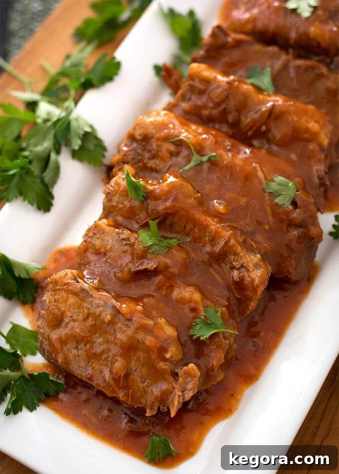 Sliced Saucy Beef Brisket on white rectangular platter garnished with green herb
