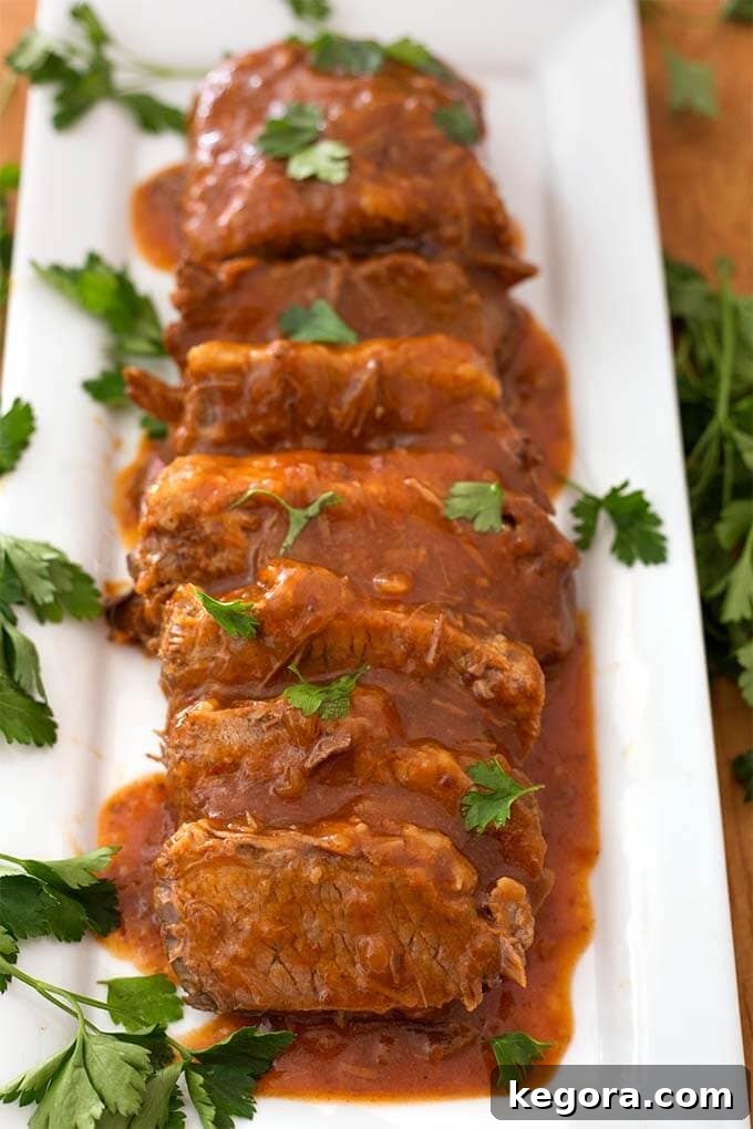 Sliced Saucy Beef Brisket on white rectangular platter garnished with green herb