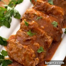 Sliced Saucy Beef Brisket on white rectangular platter garnished with green herb