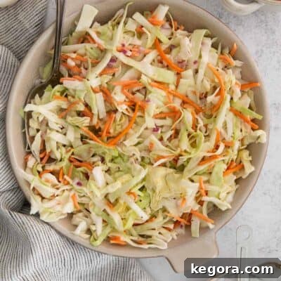 A serving of dairy-free coleslaw in a white bowl with a spoon.