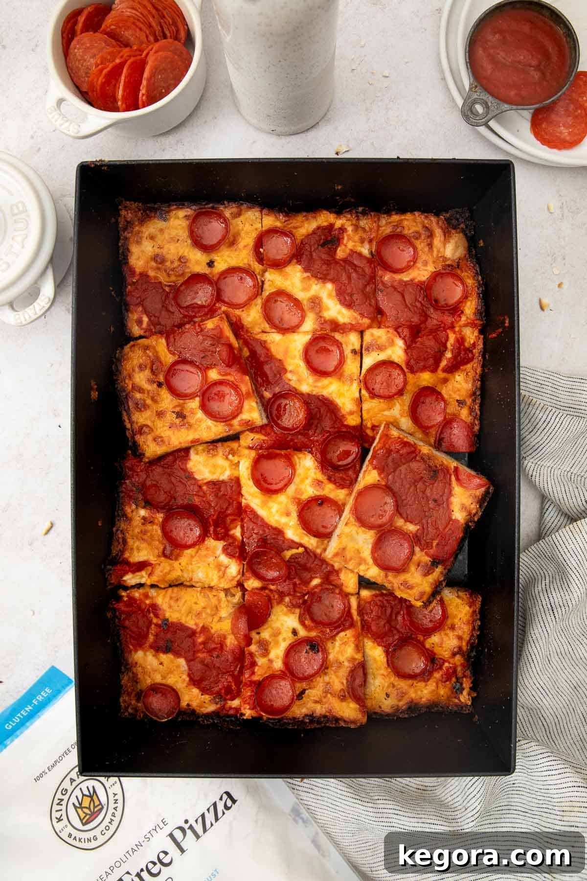 sliced gluten-free detroit-style pizza in a pan with ingredients surrounding it.