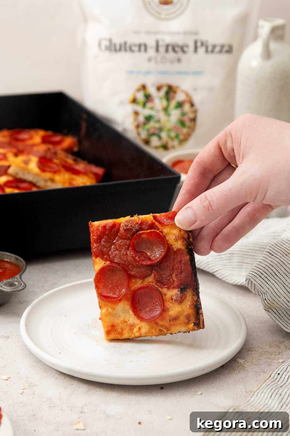 slice of gluten-free Detroit-style pizza held up on a plate by a hand.