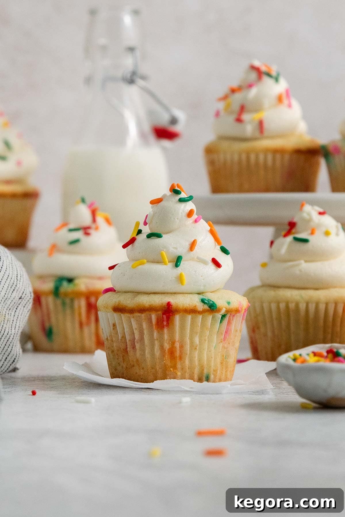 Close-up of frosted funfetti cupcakes with sprinkles, with more blurred cupcakes in the background.