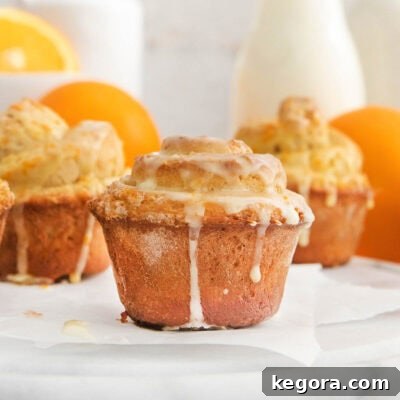 Three glazed gluten-free orange rolls, with oranges and a glass of milk in the background, ready to be enjoyed.