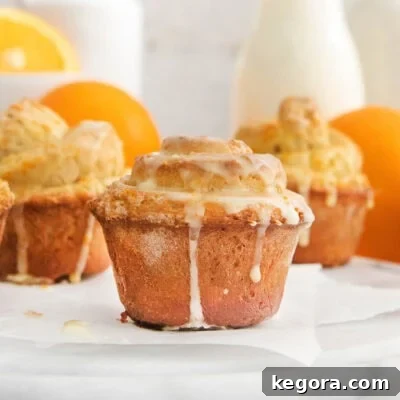 Zesty Gluten-Free Orange Buns 11 Close-up of freshly glazed gluten-free orange rolls with oranges and milk subtly blurred in the background, highlighting the inviting textures and colors.