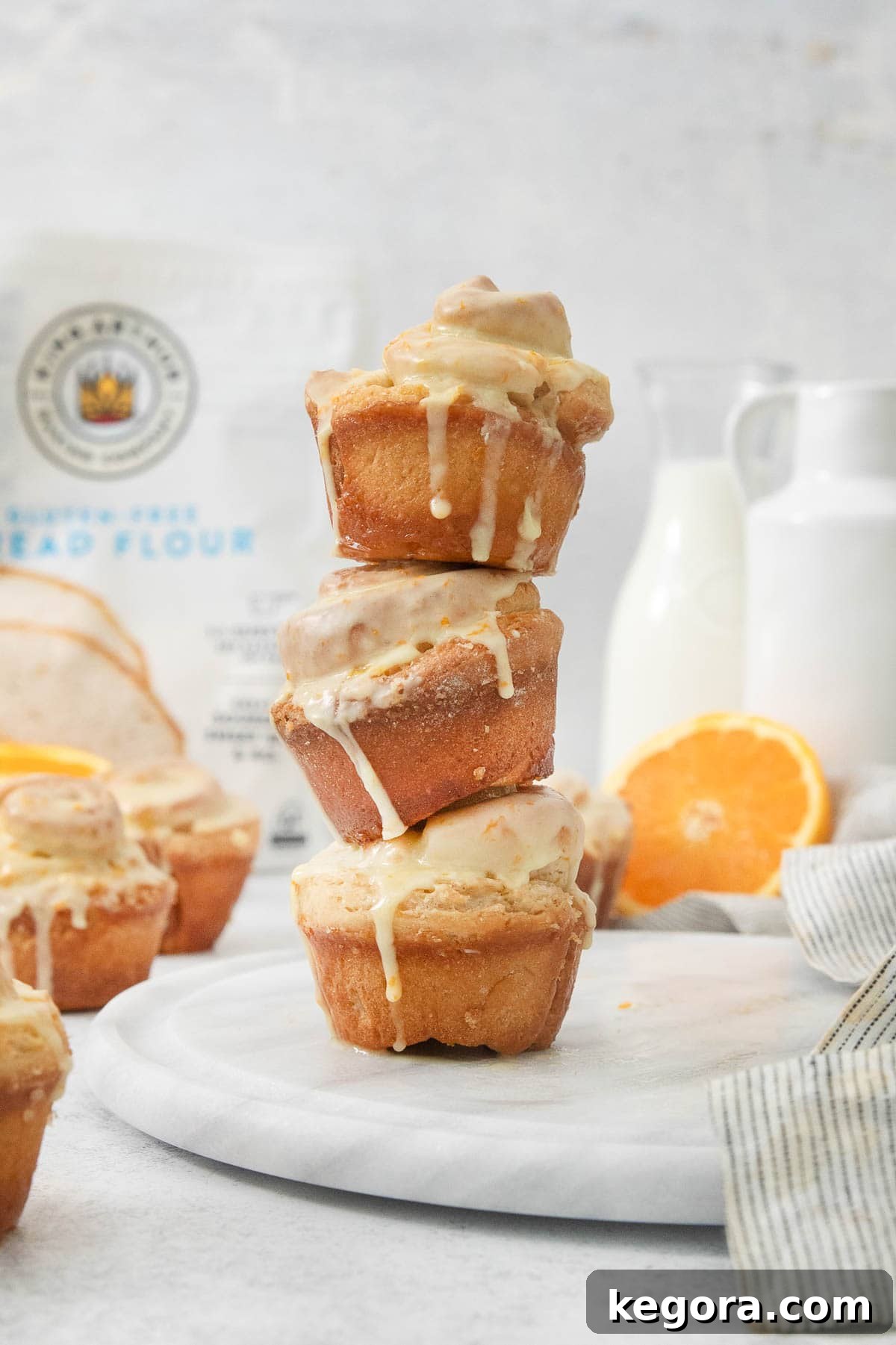 Zesty Gluten-Free Orange Buns 3 Three perfectly glazed gluten-free orange rolls stacked on a white platter, invitingly showcasing their fluffy texture and vibrant citrus glaze.