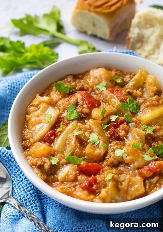 A serving of Instant Pot Unstuffed Cabbage Rolls in a white bowl with a spoon, resting on a blue kitchen towel, highlighting the rich texture and vibrant ingredients.