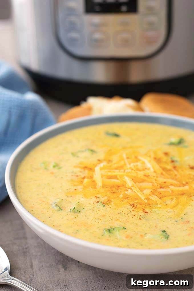 Close-up of Instant Pot Broccoli Cheddar Soup in a white bowl, with the Instant Pot in the background, showcasing its rich color and inviting texture.