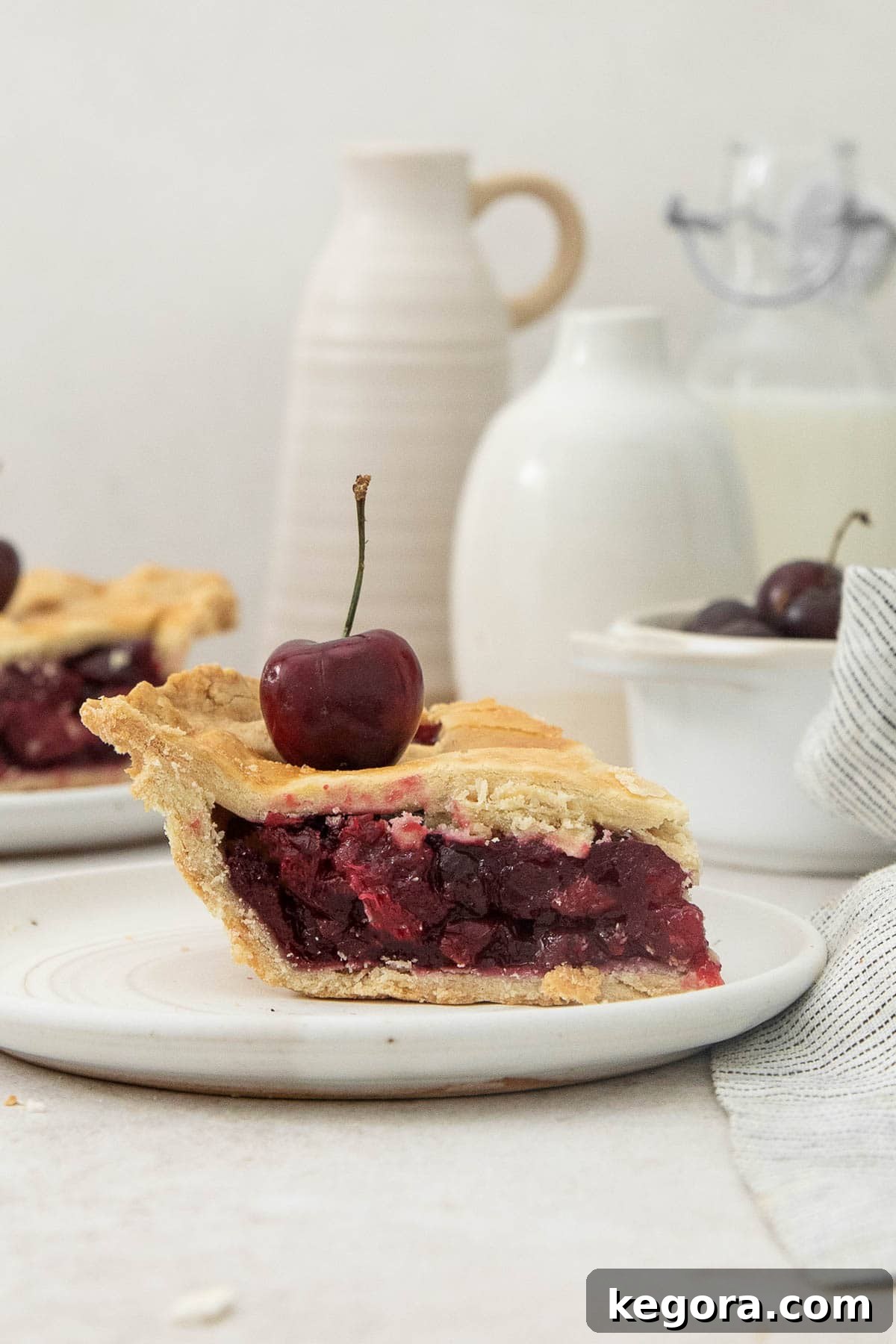 Crimson Cherry Dream 3 A perfectly sliced piece of Gluten-Free Cherry Pie, showcasing the flaky crust and rich red filling, served on a white plate with a fresh cherry garnish.