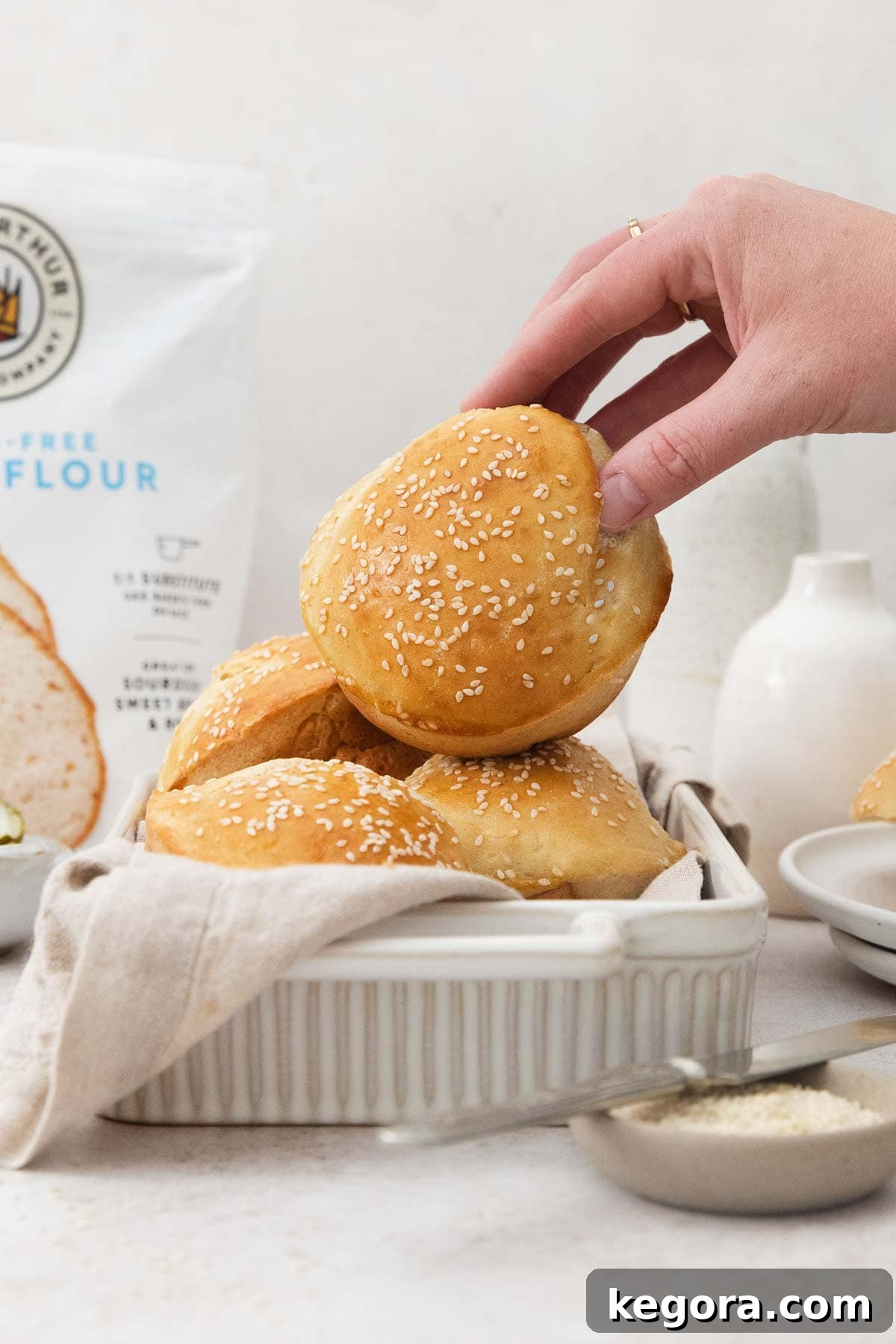 Fluffy Gluten-Free Burger Buns 3 Gluten-free hamburger buns arranged beautifully in a white serving dish, with one bun held upright to showcase its perfect golden crust and fluffy texture.
