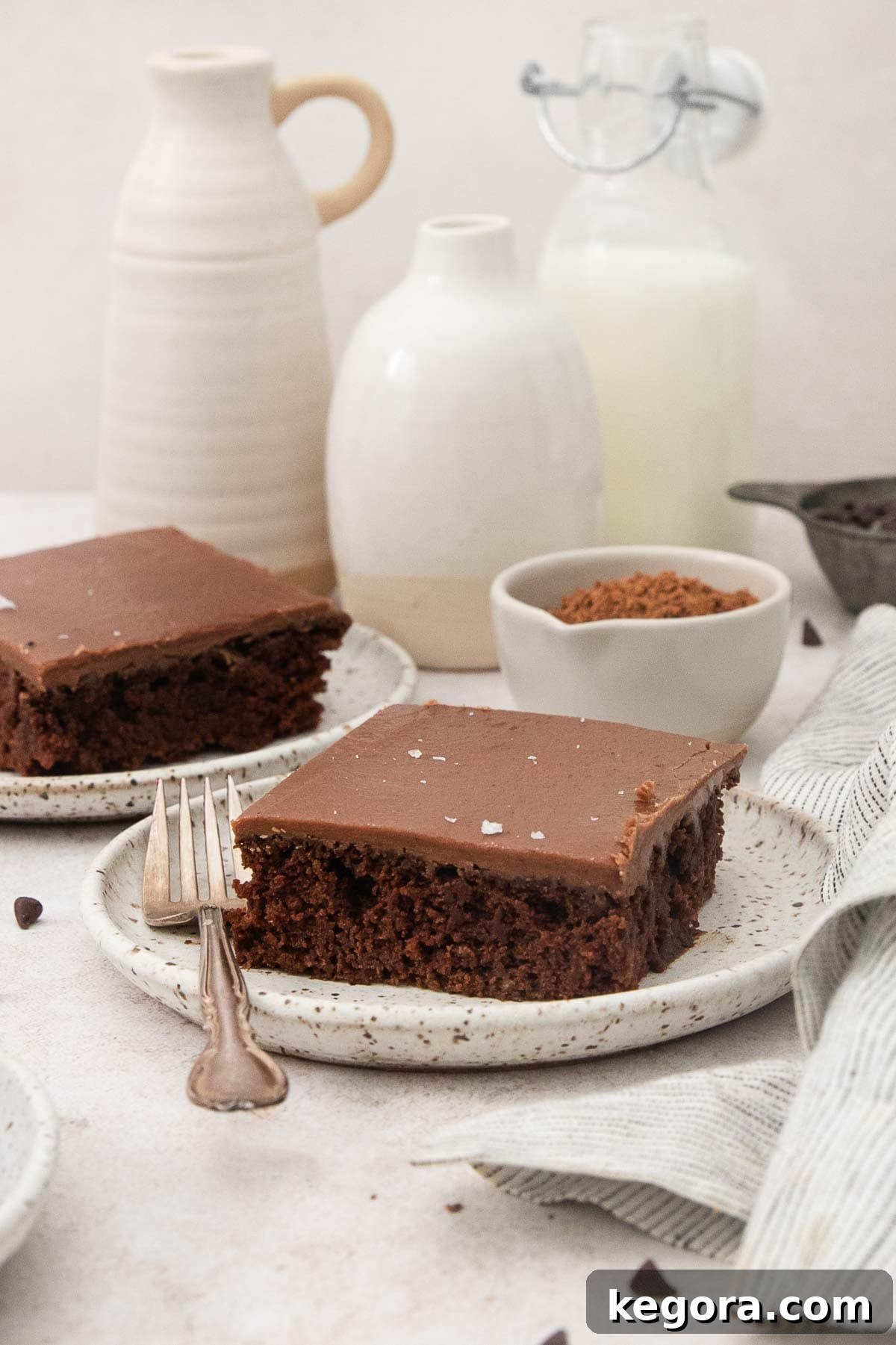 Decadent Gluten-Free Texas Sheet Cake 3 Two generous slices of rich gluten-free Texas sheet cake, featuring a dark fudgy frosting, are presented on separate speckled plates, ready to be enjoyed. A fork rests beside one slice.