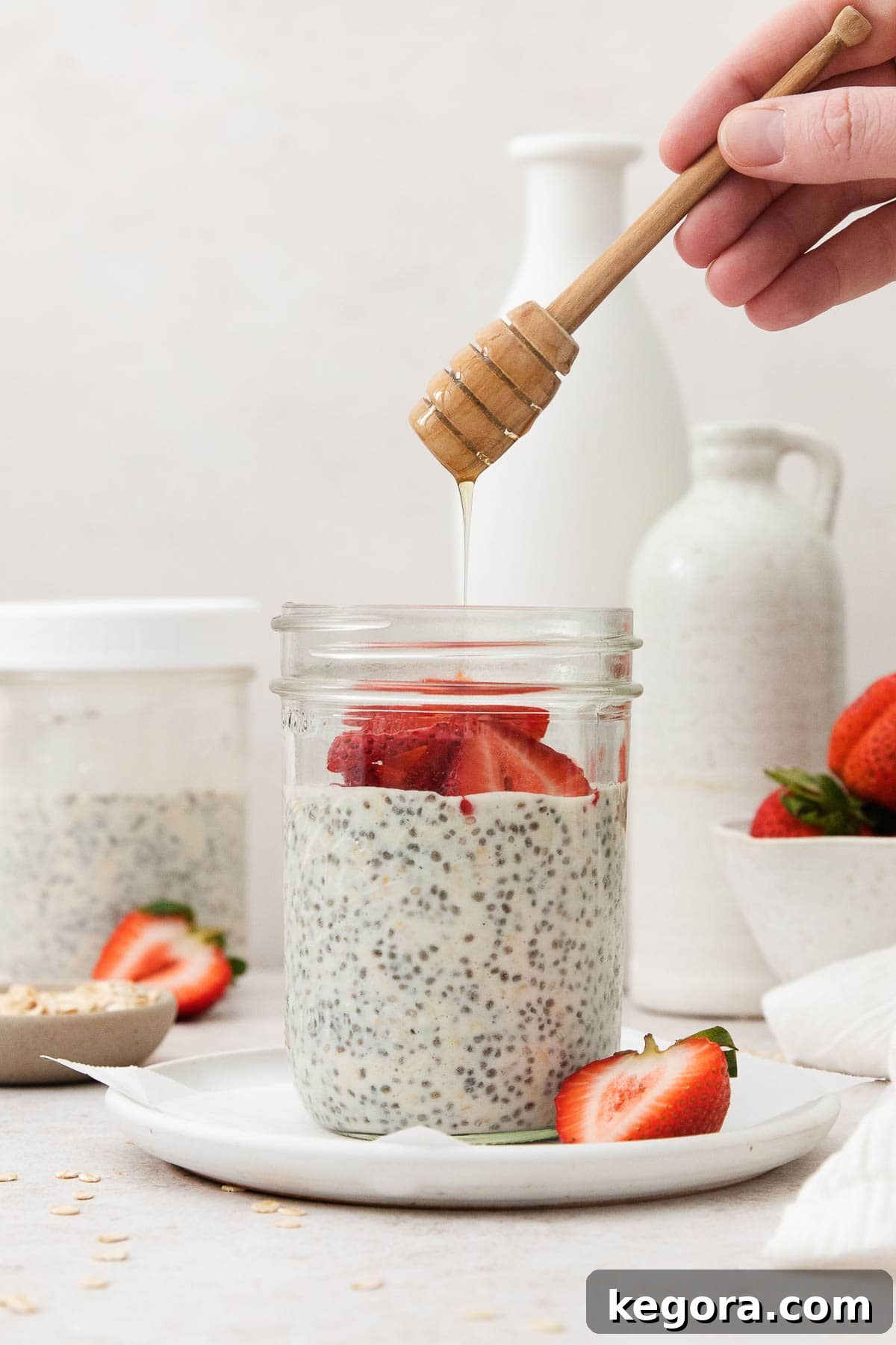 Overnight Protein Oats with Strawberries and Honey Honey being drizzled into a glass jar of overnight oats, garnished with fresh strawberry slices and whole oats.