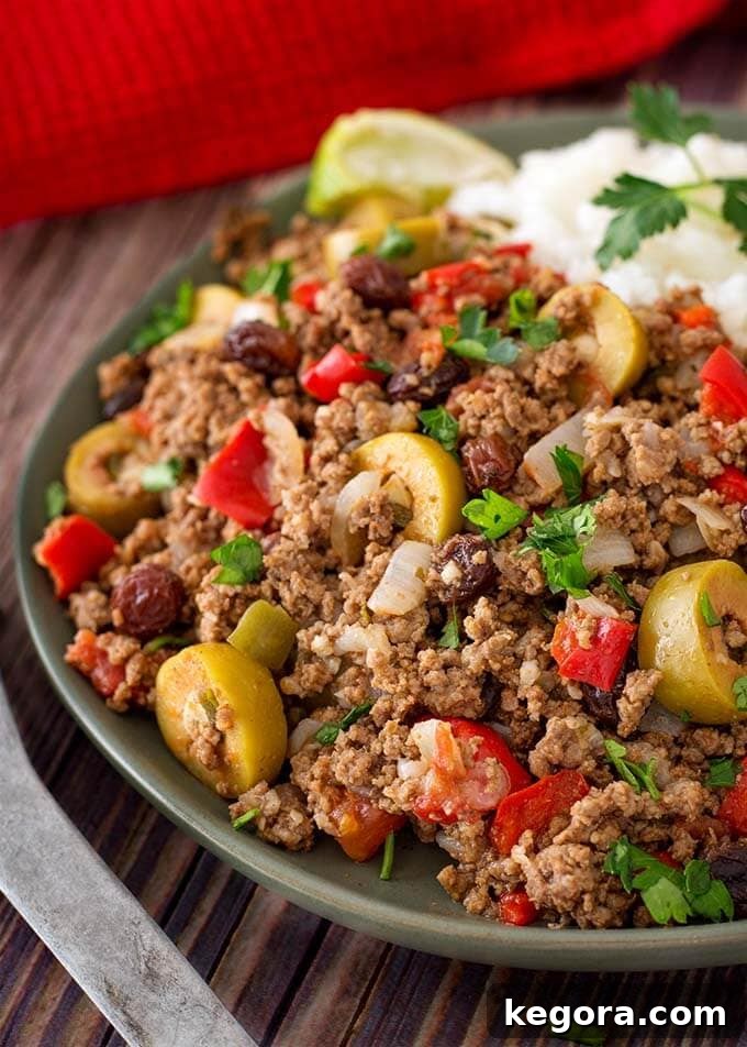 Close-up of Instant Pot Picadillo with white rice, garnished on a dark green plate next to a shiny silver spoon