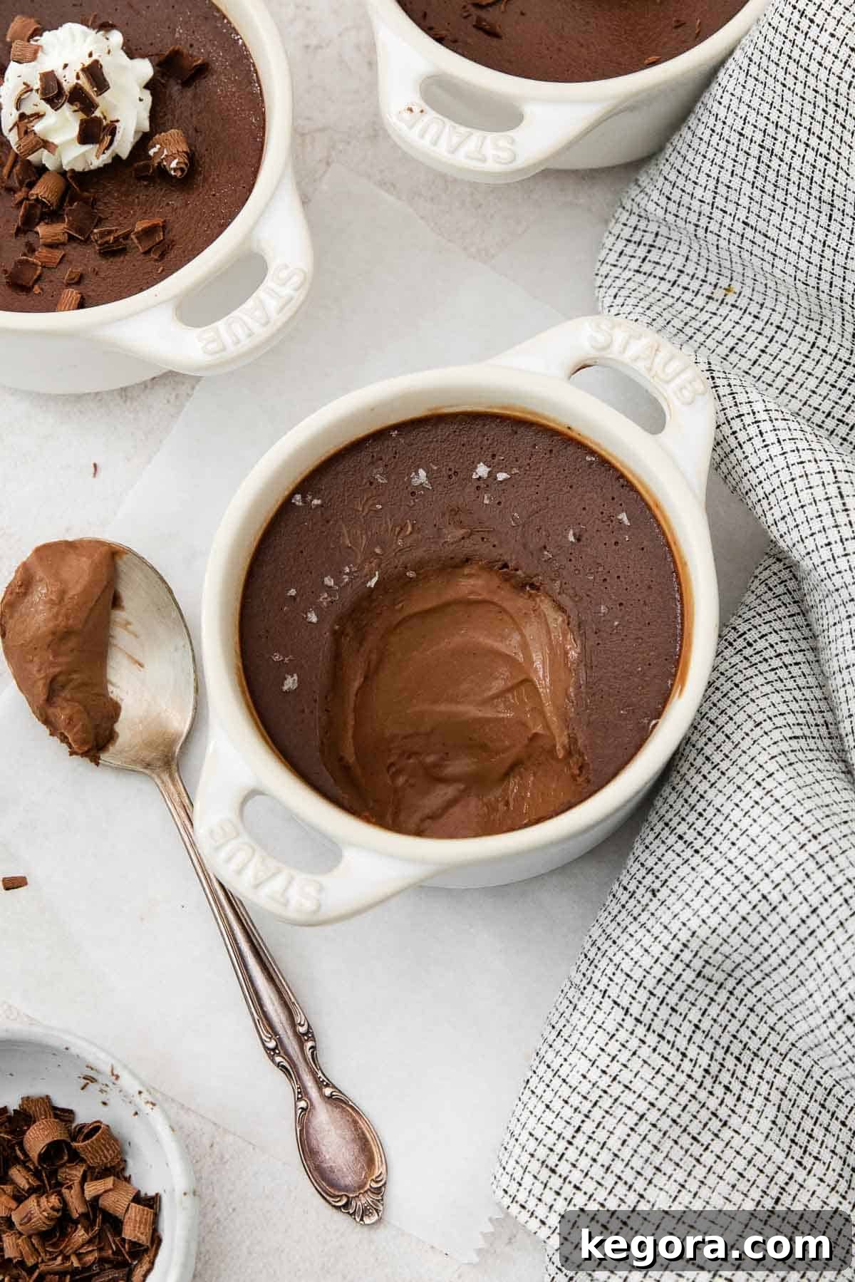 Decadent Dark Chocolate Pots 3 A spoon with a scoop of dark chocolate pot de crème, garnished with chocolate shavings, next to the ramekin.