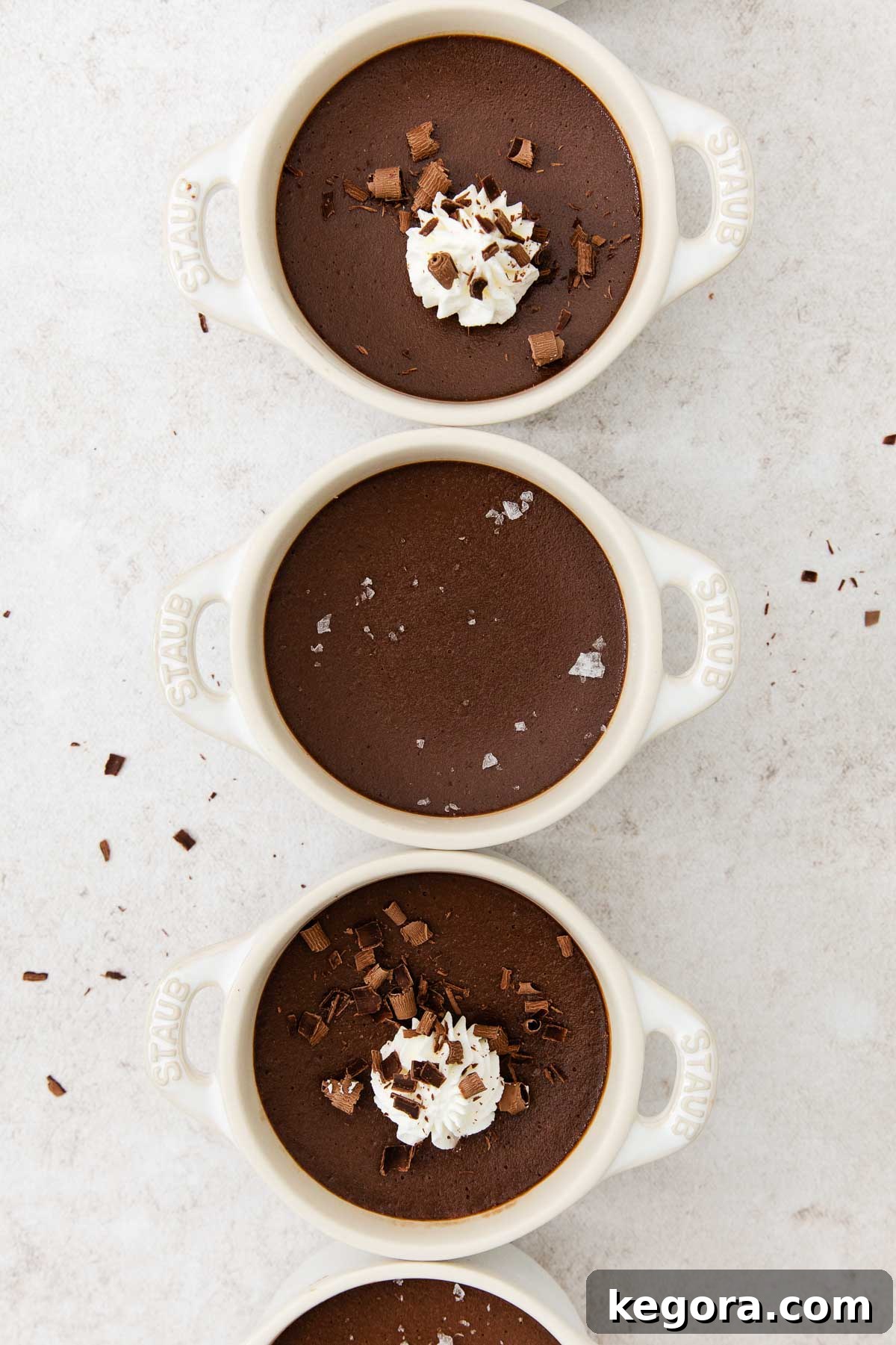 Decadent Dark Chocolate Pots 7 Overhead view of several dark chocolate pot de crème desserts, some topped with whipped cream and chocolate shavings.