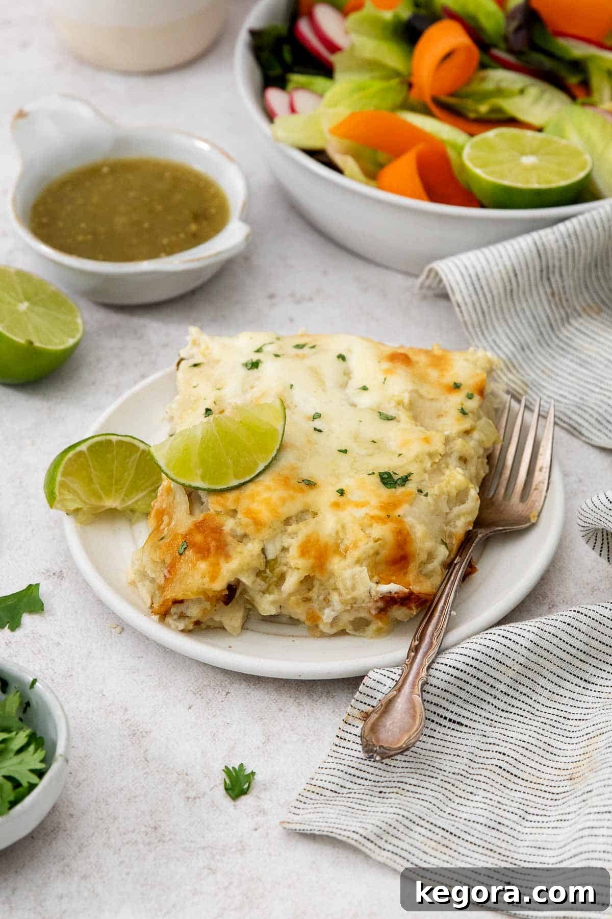 A generous serving of green chicken enchiladas on a ceramic plate, garnished with fresh lime wedges and a fork, highlighting its savory appeal.