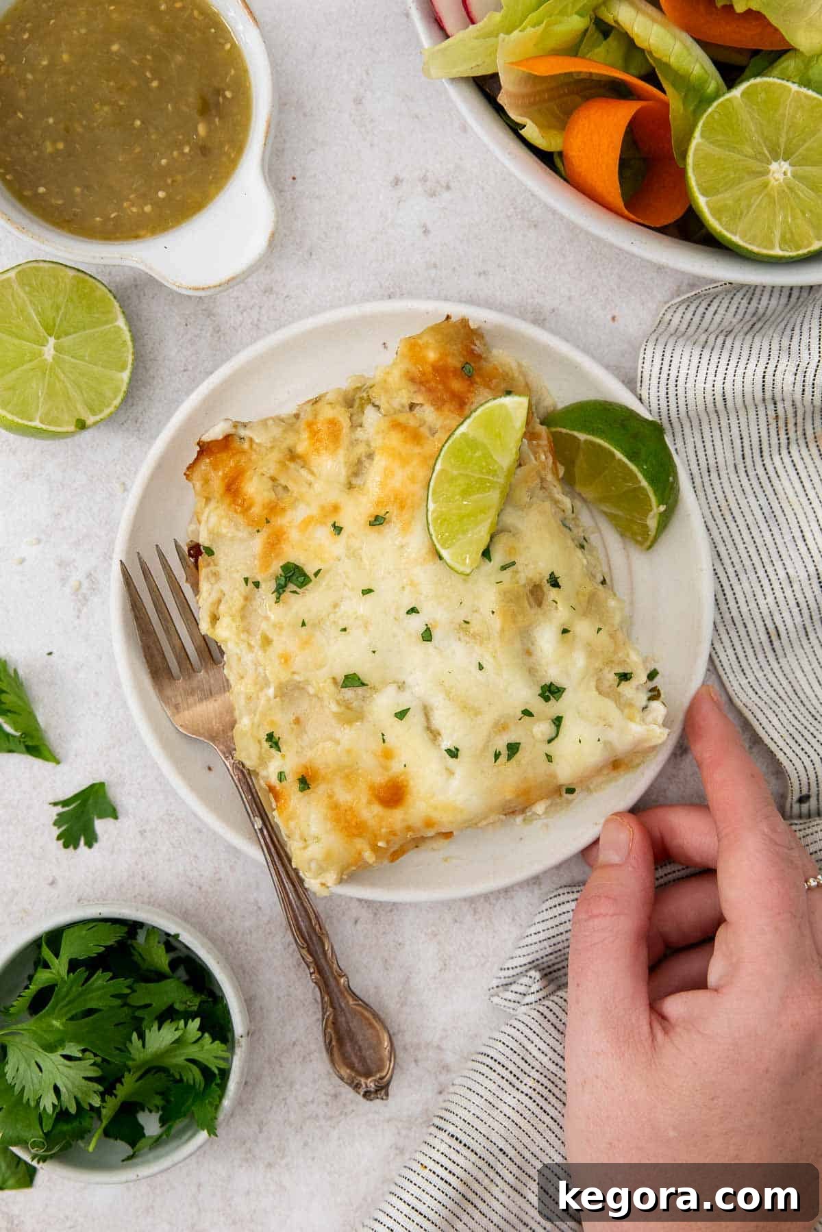 A beautifully plated serving of green chicken enchiladas, complete with fresh lime wedges and a fork, ready to be enjoyed.