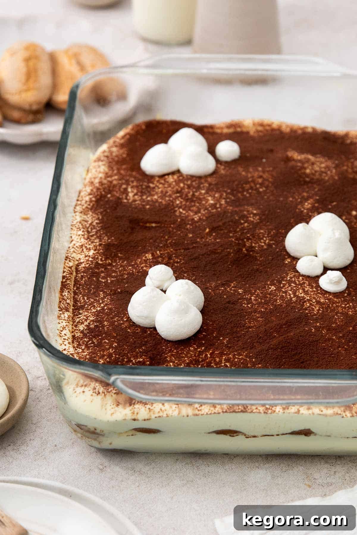 A beautiful side view of a layered gluten-free tiramisu setting in a glass baking dish, showing the distinct alternating layers of cream and coffee-soaked ladyfingers, ready to be served.