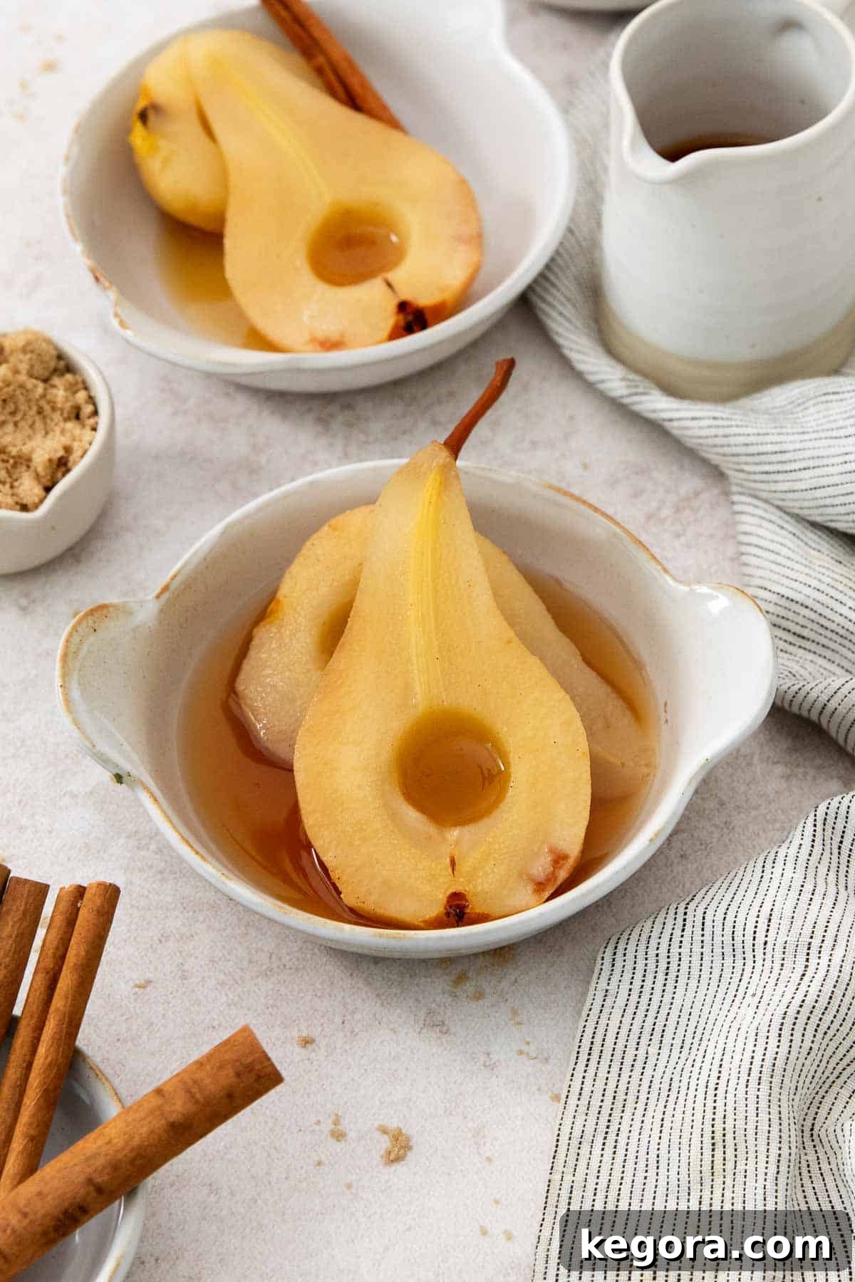 Two beautifully poached pears nestled in a dish, glistening with apple cider syrup.