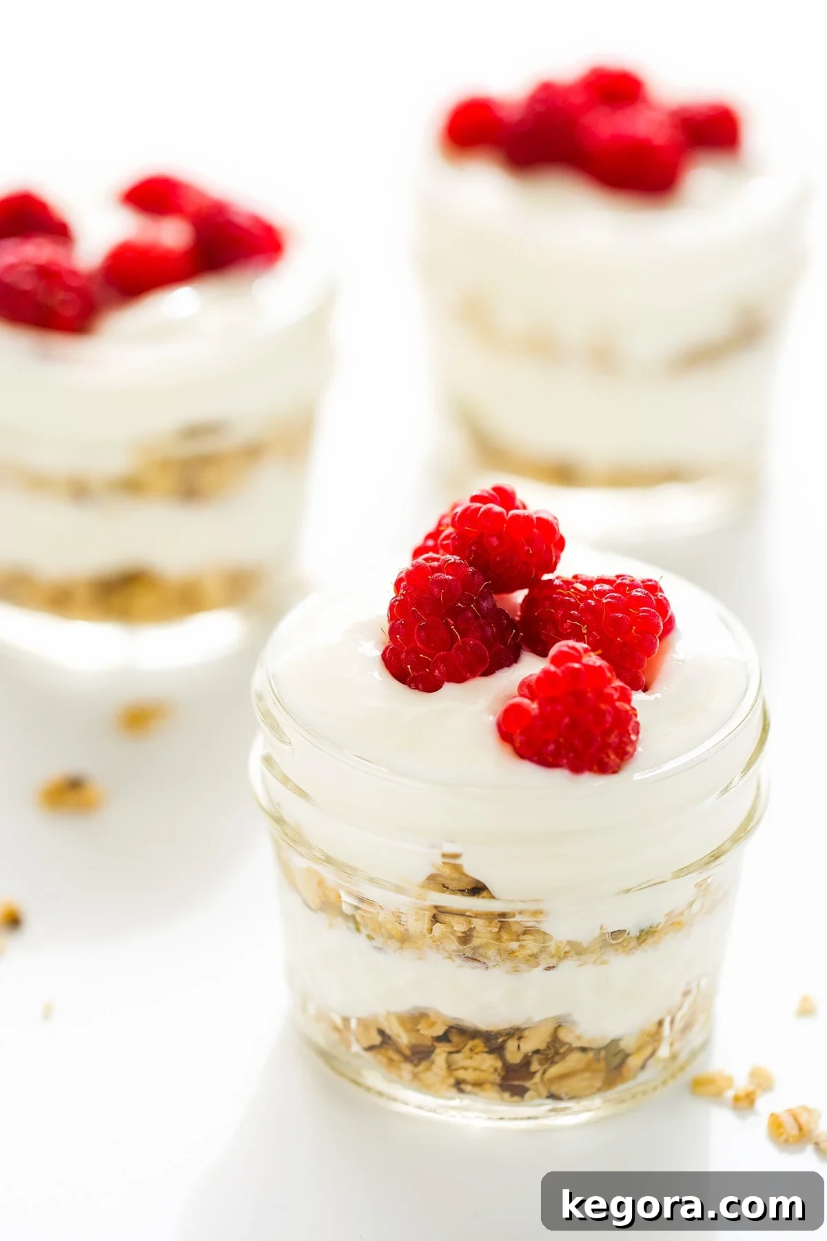 Effortless Instant Pot Yogurt 5 Three glass jars layered with granola and yogurt topped with raspberries, perfect for a parfait.