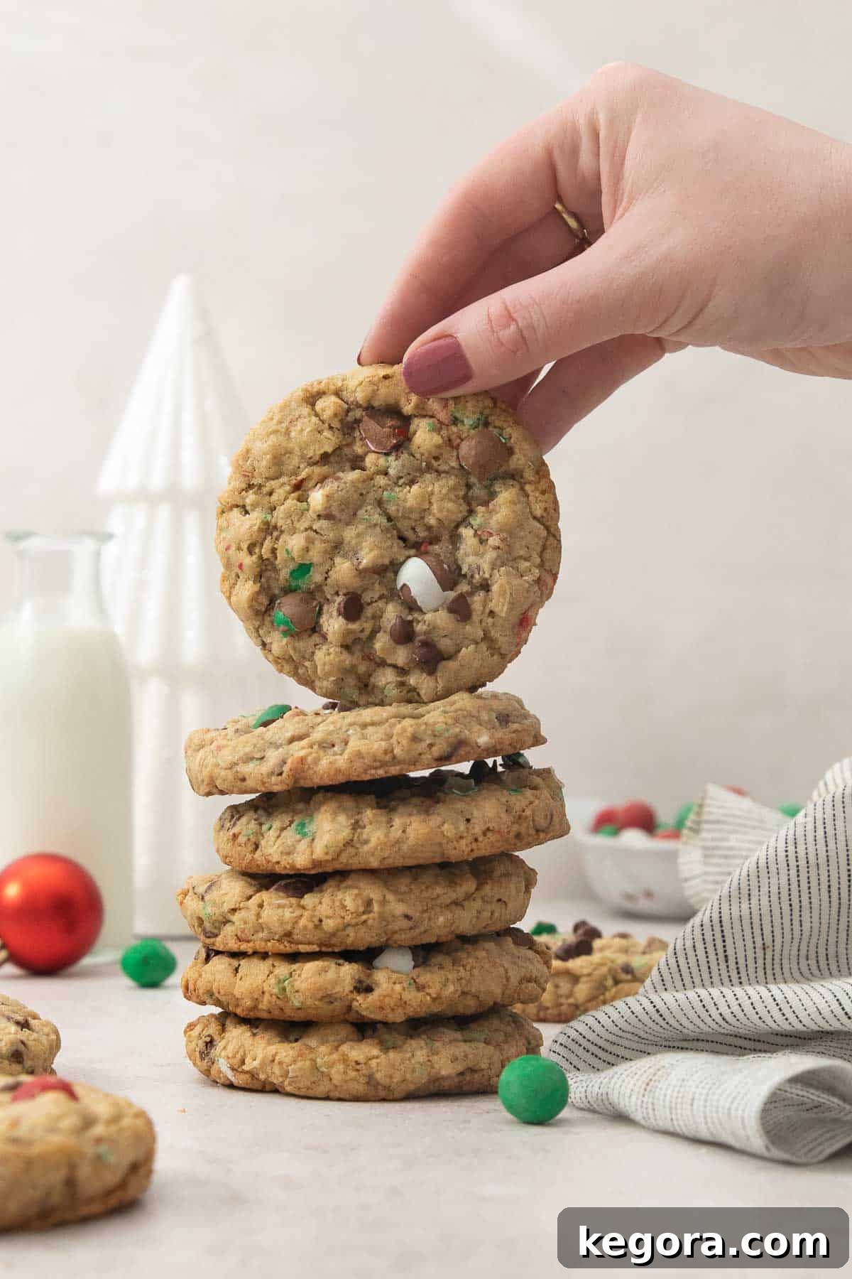 A hand holding up one Cadbury Snowball cookie, artfully stacked above a tower of additional cookies, showcasing their inviting texture and festive appearance.