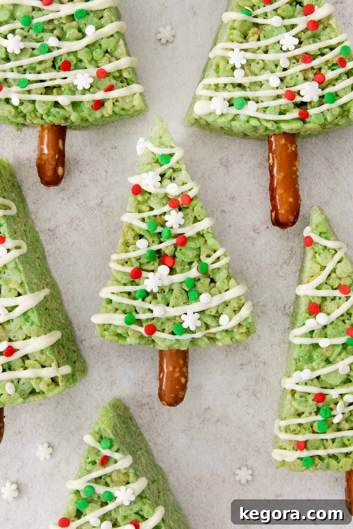 A delightful display of beautifully decorated Christmas tree crispy treats arranged appealingly on a festive white countertop, glistening with sprinkles and ready for serving.