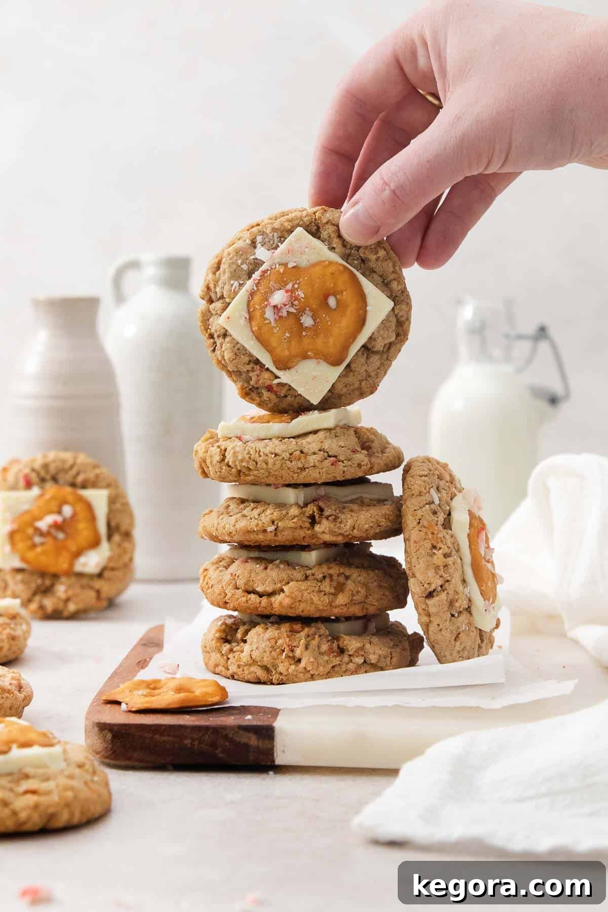 A hand holding up one white chocolate peppermint pretzel cookie on top of a stack of cookies.