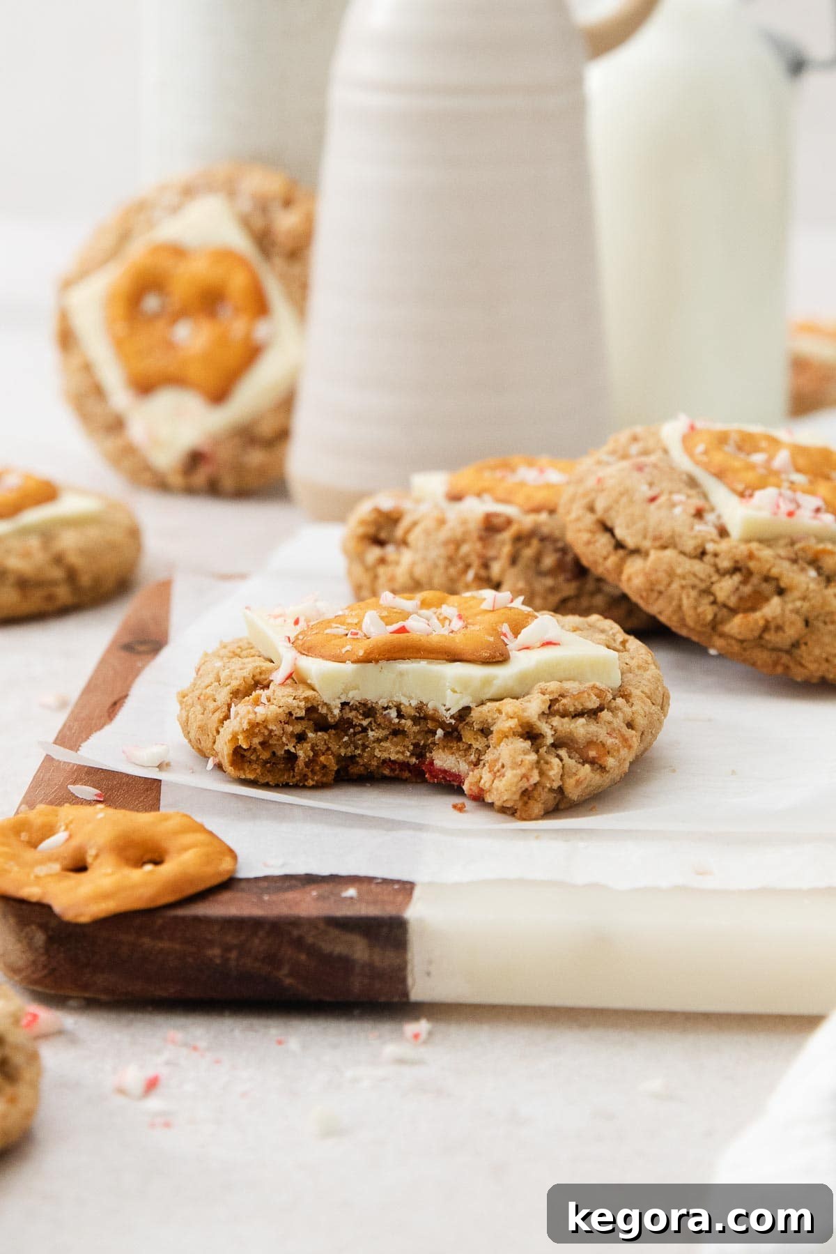 One white chocolate peppermint pretzel cookie with a bite missing, with more cookies in the background.