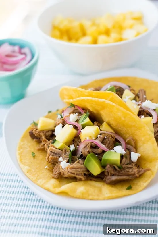 Close-up of succulent pineapple chipotle pork tacos garnished with fresh cilantro and a side of vibrant pickled onions, served on a crisp white plate with a striped napkin.