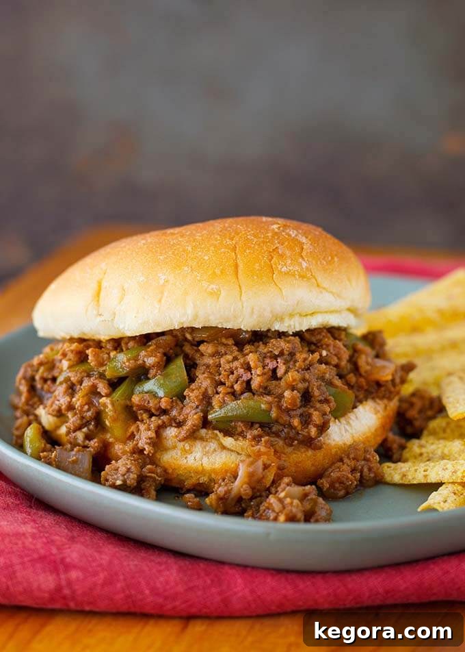 Easy Instant Pot Sloppy Joes 2 Sloppy Joes on a soft hamburger bun, served with a side of crispy potato chips on a blue plate.