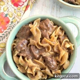 Beef and Noodles in turquoise bowl with handles on light wood background