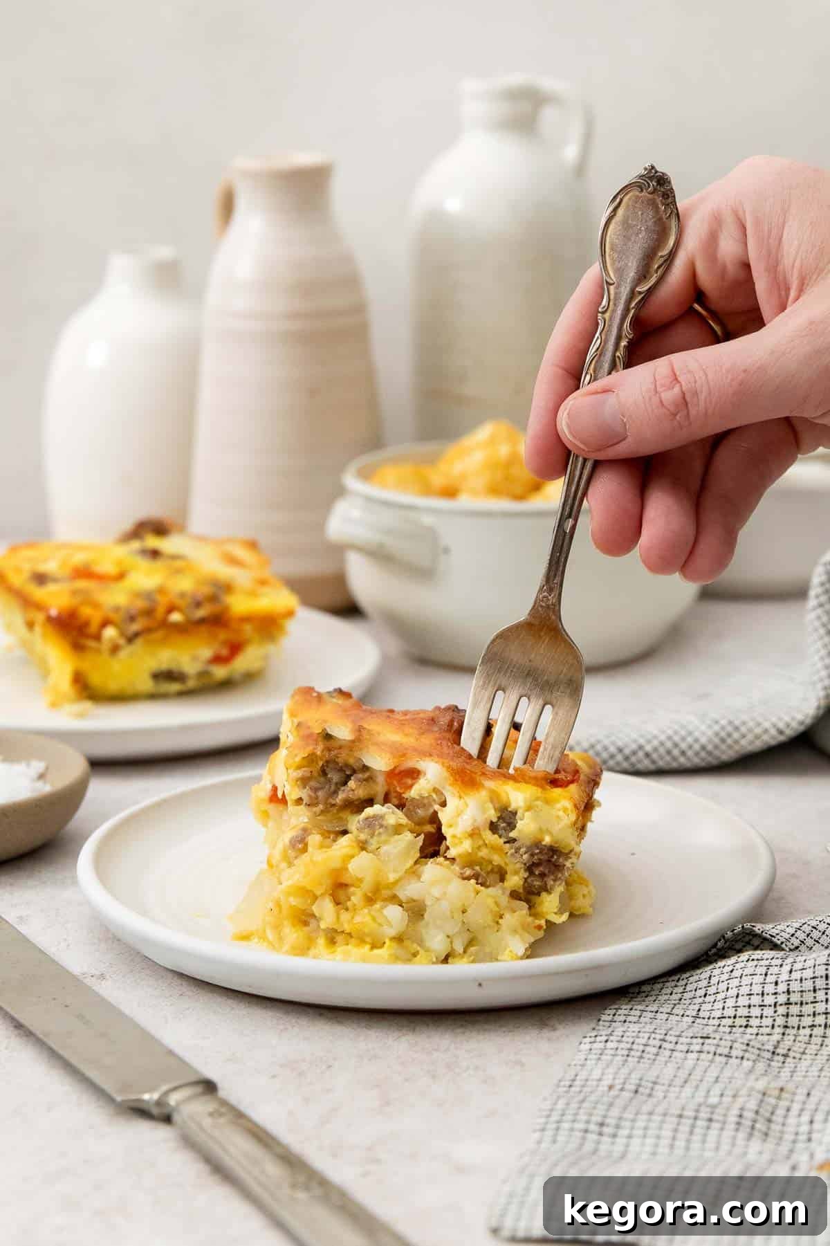 A fork being stuck into a slice of golden-brown gluten-free tater tot breakfast casserole, highlighting the crispy tater tots, savory sausage, and melted cheese within a fluffy egg base.