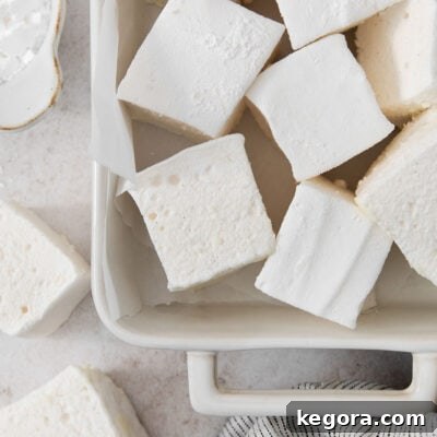 A cropped photo of fluffy homemade vanilla bean marshmallows in a baking dish, perfectly cut and ready to be enjoyed.